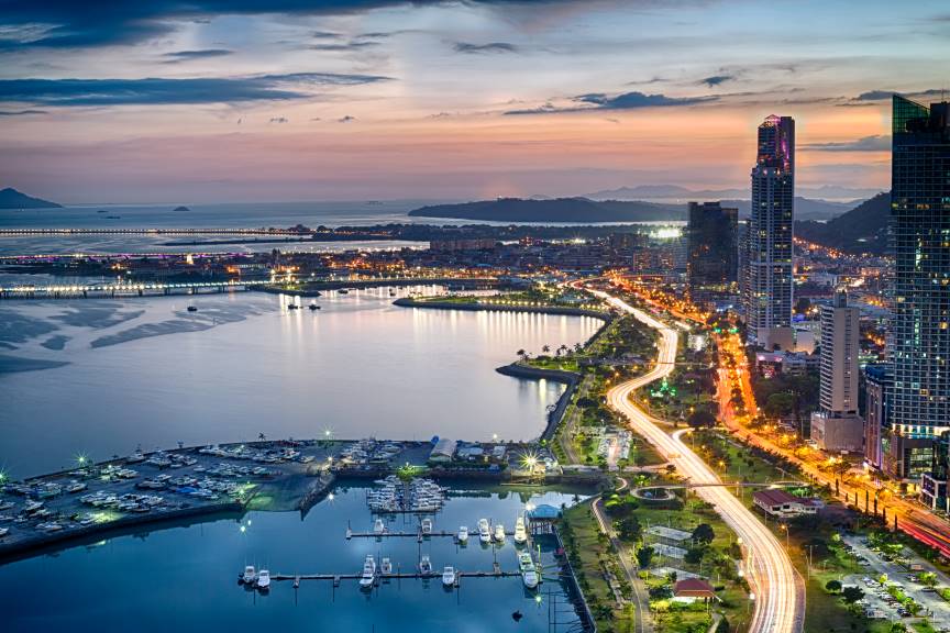 Panama City skyline at sunset, showcasing modern buildings, a scenic coastline, and vibrant city lights reflecting off the water, illustrating the dynamic urban life for those relocating to Panama from the USA.