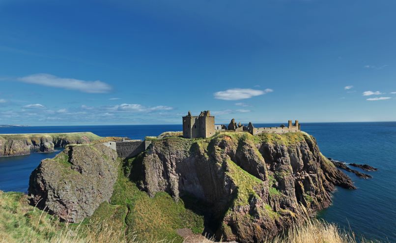 A scenic view of Dunnottar Castle, an ancient stone fortress located on a cliff overlooking the sea in Scotland, with the blue waters of the North Sea in the background.