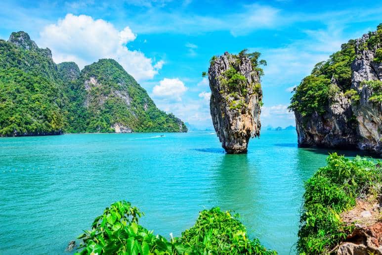 A serene view of a towering limestone rock formation surrounded by turquoise waters in Phuket, Thailand, representing the country's picturesque landscapes, tropical climate, and appeal as a relocation destination.