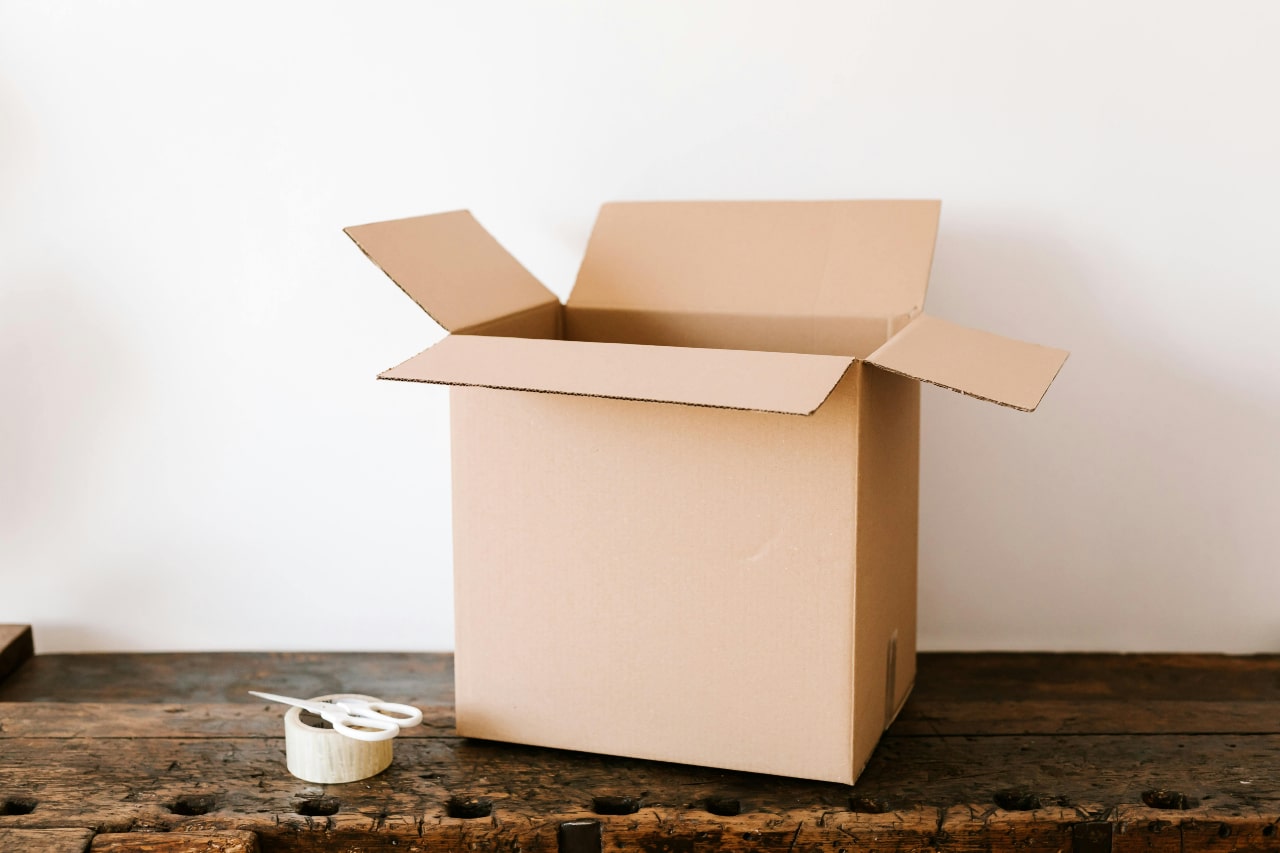 An empty cardboard box on a rustic wooden table with packing tape and scissors.