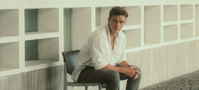 A young man in a relaxed pose outside a modern white building, representing the intersection of style and architecture.