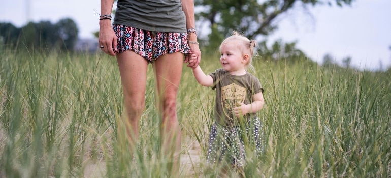 A mother, raising a family in Iceland, and her young daughter walk through a field of tall grass, holding hands and sharing a special moment in nature.