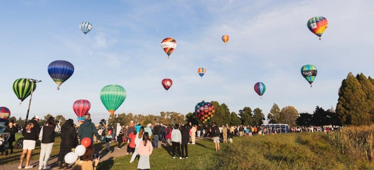 Crowds gather under colorful hot air balloons at a festival, celebrating the vibrant community spirit in New Zealand.