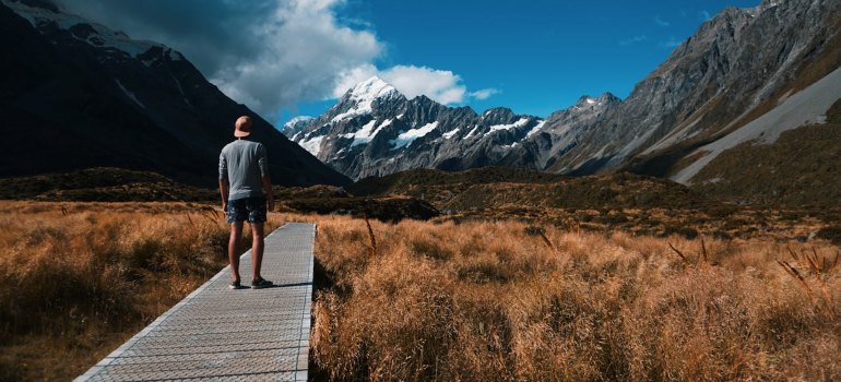 A man walks a boardwalk surrounded by stunning mountain views in New Zealand, ideal for family exploration.